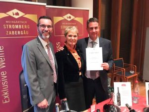 Man sieht J&uuml;rgen Conz, Vorstandsvorsitzender der WG Stromberg-Zaberg&auml;u, Friedlinde Gurr-Hirsch, politische Staatssekret&auml;rin im Ministerium f&uuml;r L&auml;ndlichen Raum und Verbraucherschutz und Dr. Bernd Kost, Gesch&auml;ftsf&uuml;hrer der WG Stromberg-Zaberg&auml;u. Er h&auml;lt die Urkunde zum Staatsehrenpreis, den er soeben empfangen hat, in H&auml;nden.