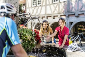 Radfahrer machen Pause an einem Brunnen, in der Region Kocher - Jagst - Tauber.