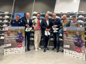 Trollinger Marathon 2025: Holger Braun, Harry Mergel, Thomas Grabert, Alexander von Preen, Steffen Schoch, Torsten Scholze und Ariane Pakaki-Buchner stehen vor dem Sportschuhe-Regal.